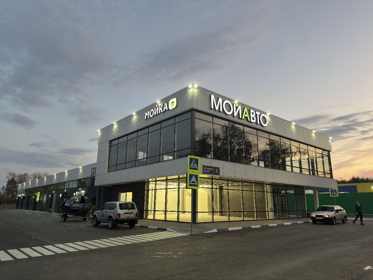 Здание мойки «Мой Авто» вечером: светится вывеска, вдоль фасада боксы